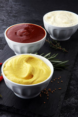 Classic set of sauces in white saucers: American yellow mustard, ketchup, mayonnaise