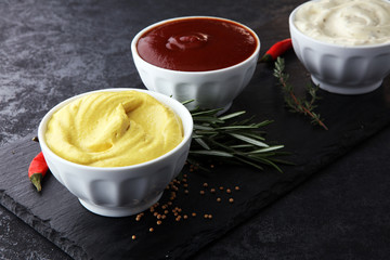 Classic set of sauces in white saucers: American yellow mustard, ketchup, mayonnaise