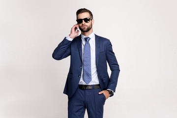 Important call. Handsome young man sunglasses talking on mobile phone while standing against white background. - Powered by Adobe