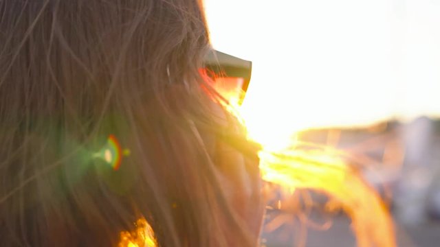 Woman in sunglasses using smartphone while walking down a dock with a lot of yachts and boats at sunset, close-up