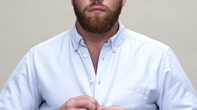Cropped close up view of bearded man puts on his shirt over gray background