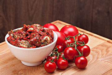 Sun dried tomatoes in white bowl and heap of ripe fresh tomatoes .