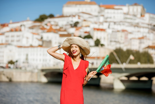 Portrait of a young woman tourist in red dress standing with portuguese flag on the Coimbra city background in central Portugal