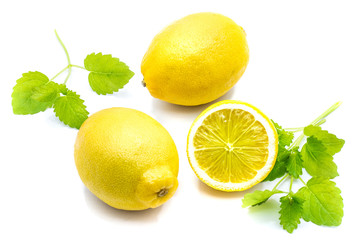 Pair of whole yellow lemons, cross section half and fresh green lemon balm leaves isolated on white background .
