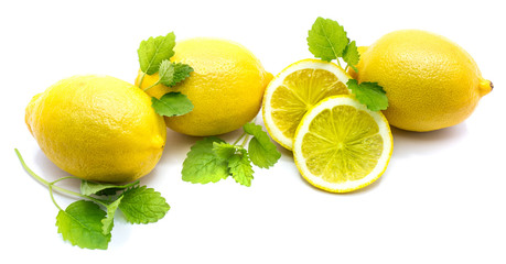 Composition of three whole lemons and two slices on fresh green lemon balm leaves isolated on white...