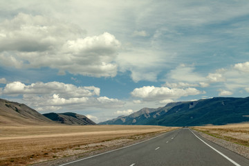 highway between mountains and a blue sky with large clouds