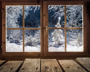 Blick aus einer Holzhütte auf einen Winterwald mit Weihnachtsbaum