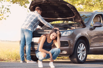 Young woman and man with broken car on background