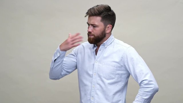 Young Confused bearded man in shirt having hot and looking at the around over gray background