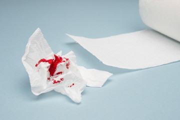 A photo of used bloody toilet paper and a tiolet paper roll on the light blue background. Hemorrhoids, constipation treatment health problems. Menstrual, hemorrhoids bleeding. Blood drops and traces - 180171143
