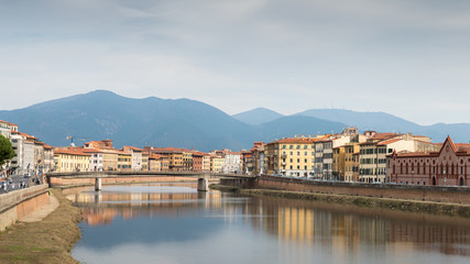 Fototapeta na wymiar Ancient house with tower overlooking River Arno in Pisa, Tuscany, Italy with Apennine mountains in background