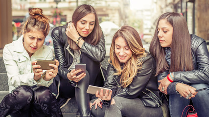 Happy girl friends sitting on the city stairs with smartphone