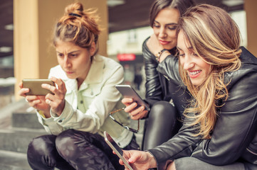 Happy girl friends sitting on the city stairs with smartphone