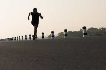 Asia young man running in the time during sunrise on dam road exercise.Healthy lifestyle