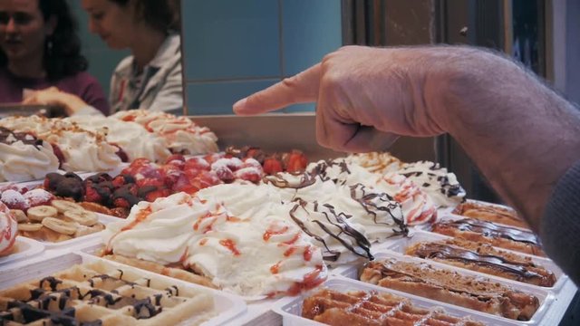 Waffles with strawberry and cream in shop, woman choose different waffles in brussels cafe