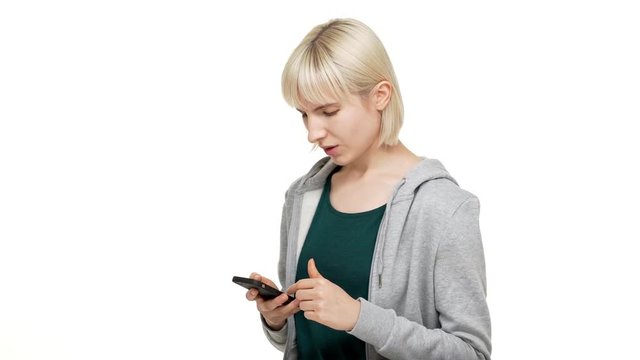half-turn portrait of happy caucasian woman 20s wearing casual clothes holding using smartphone scrolling feed finding good news thowing thumb up like sign over white background. Concept of emotions