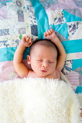 New Baby Boy sleeping wrapped in fluffy cream blanket on pathwork quilt