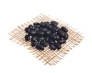 Black turtle Bean. Grains over hessian fabric, isolated white background.