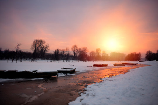 Beautiful winter sunset at the river. The boat in snow at the river in the winter