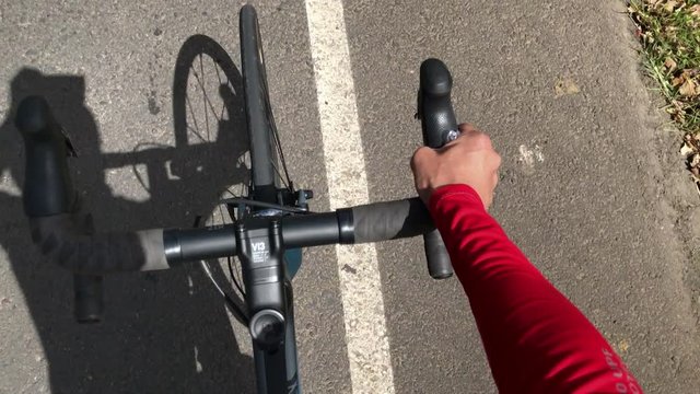 Cyclist pedaling. Point of view of cyclist on the road riding with one hand.