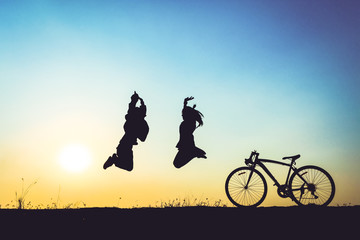 silhouette of young woman and boy jumping on sunset sky with bicycle on the prairie at yellow evening horizon sea yellow sunset heaven background Outdoor.