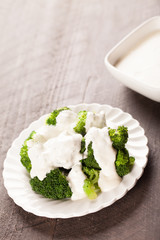 
Stack of broccoli drizzled with creamy white sauce on top of antique plate with dark wooden background slightly above shot
