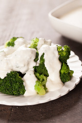 
Stack of broccoli drizzled with creamy white sauce on top of antique plate with dark wooden background vertical shot
