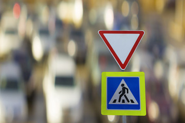 Traffic signs give way and pedestrian crossing on background of the cars.