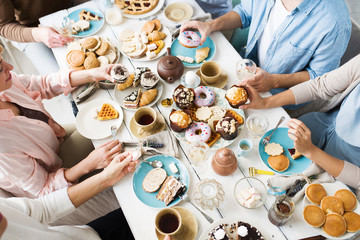 Friends gathered for birthday celebration having fresh homemade puffs and pastry with tea by served table