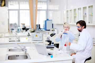 Man and woman in whitecoats analyzing liquid chemical substances