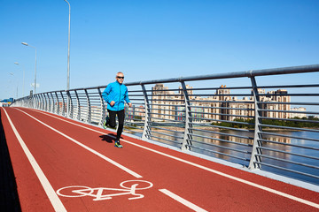 Mature sprinter running along bridge railings by riverside in urban environment
