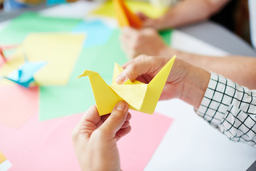 Human hands folding sheet of yellow paper while making origami bird - obrazy, fototapety, plakaty