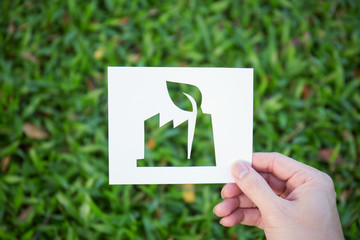 Hands holding cut paper with the logo of factory shape over green glass background. friendly green living. Sign and symbol background banner template of environment friendly concept. Earth day
