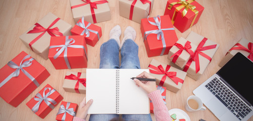 Hands holding pen whiting on notebook making gift list with Christmas gift box top view, Celebrate Christmas holiday online shopping background and banner concept.