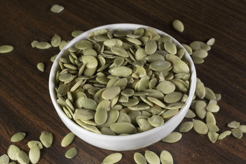Vegan food. Raw pumpkin seeds for roasting in a white dish. Wooden background.