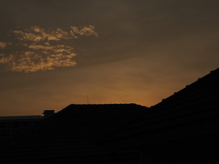 Sunset dark black and yellow orange clear sky with silhouette shadow of village house roof, and small clouds background