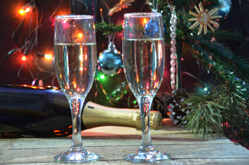 a bottle of champagne and glasses on the background of a Christmas tree decorated with balls and New Year's lights. happy christmas concept. Ribbon, baubles and wine against Christmas lights