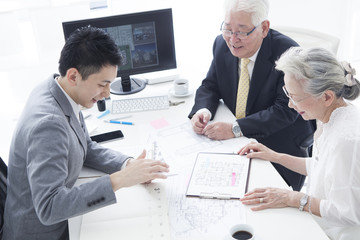 A sales clerk and an elderly couple are talking while looking at the plan