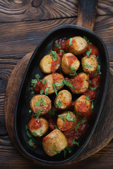 Baked potatoes cooked in sicilian style and served in a metal plate, top view in a rustic wooden setting