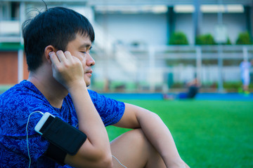 Asian sport man is listening his favorite song by smart pohne that hold on his arm during relax in sport ground.