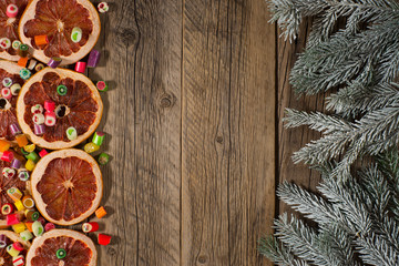 Fir tree branch with orange, grapefruit and candy on an old wooden table.