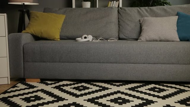 Interior of the empty cosy living room with sofa, pillows and white headphones. Home