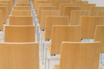 Many empty wooden chairs set neat rows in conference room
