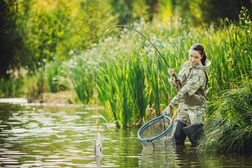 Fotobehang pretty woman fishes on the river. Spinning equipment, angling, fisherwoman concept. © kaninstudio
