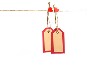Obraz na płótnie Canvas Two red and brown paper tags hanging on the rope by heart shape pin with copy space isolated on white background. St. Valentines gift concept.