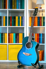 A blue guitar and a white shelf with books and a lamp