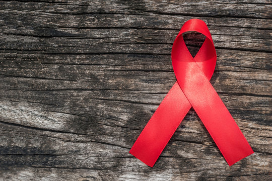 Aids Red Ribbon For World Aids Day And National HIV/AIDS And Aging Awareness Month Concept With Symbolic Bow Color Isolated With Clipping Path For Copyspace  On Aged Wood