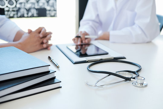 Patient listening intently to a male doctor explaining patient symptoms or asking a question as they discuss paperwork together in a consultation