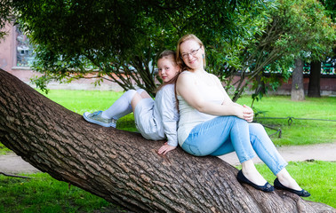 Mother and daughter are sitting on the trunk of a tree in summer Park