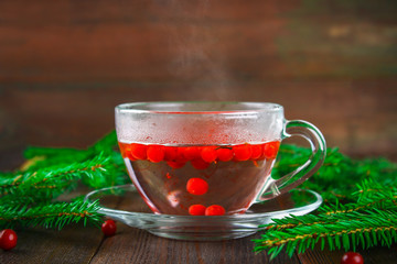 Hot tea from cranberries in a glass cup surrounded by fir branches on a wooden table.